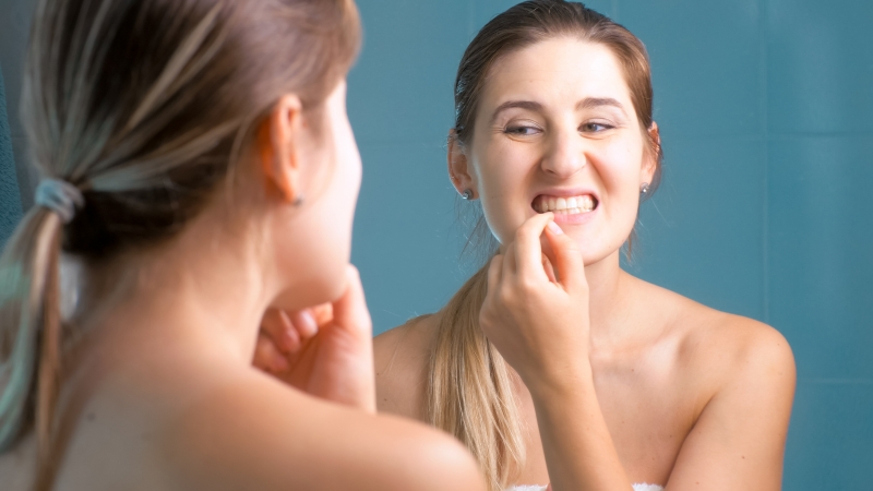 A woman looking at her teeth and gums in the mirror.
